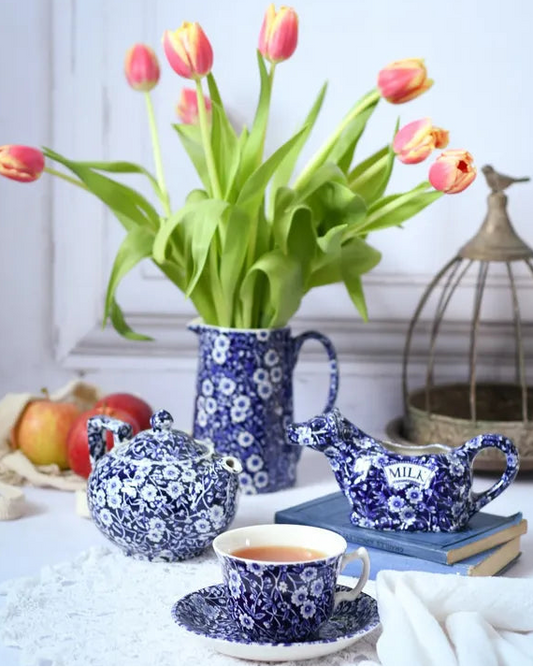 Burleighware Tea set with floral patterns including a teapot, cup, and milk pitcher, accompanied by tulips in a vase.